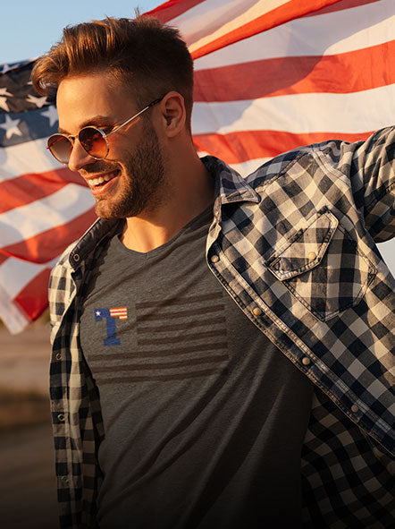 A man is wearing glasses and a USA flag design t-shirt with US flag flattering behind